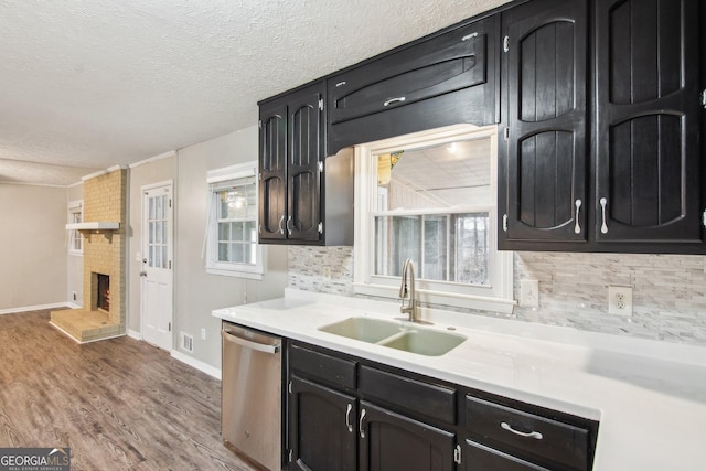 kitchen featuring dishwasher, wood finished floors, light countertops, a fireplace, and a sink