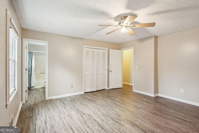 unfurnished bedroom featuring baseboards, connected bathroom, wood finished floors, a textured ceiling, and a closet