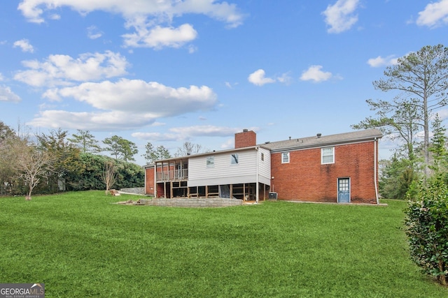 rear view of house featuring a deck, brick siding, a lawn, and a chimney