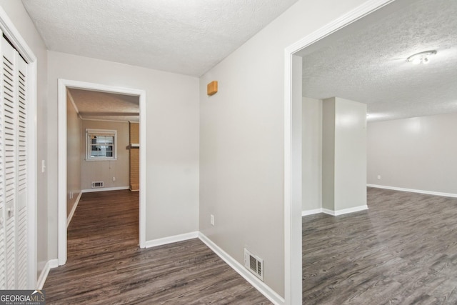 corridor featuring visible vents, a textured ceiling, baseboards, and wood finished floors