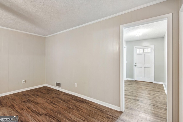 empty room with dark wood-style floors, visible vents, ornamental molding, a textured ceiling, and baseboards