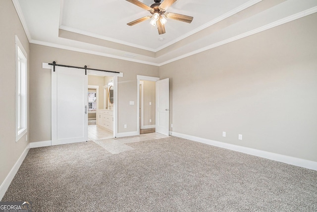 unfurnished bedroom with ensuite bath, a tray ceiling, ornamental molding, light carpet, and a barn door