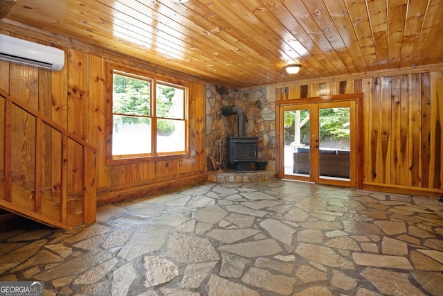 unfurnished living room with a healthy amount of sunlight, a wood stove, a wall mounted AC, and wooden ceiling