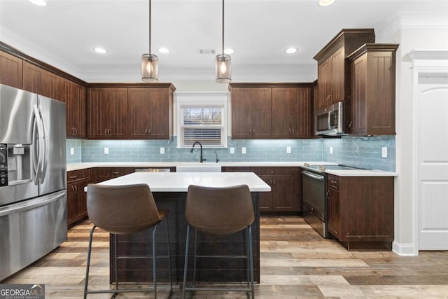 kitchen with a kitchen island, appliances with stainless steel finishes, decorative light fixtures, sink, and dark brown cabinetry