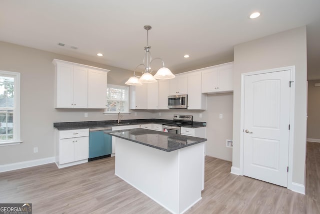 kitchen featuring stainless steel appliances, a center island, white cabinets, and decorative light fixtures