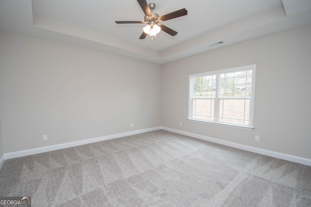 empty room featuring ceiling fan, carpet flooring, and a tray ceiling