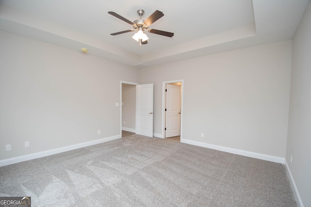 carpeted empty room with a raised ceiling and ceiling fan