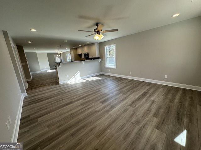 unfurnished living room featuring dark wood-type flooring and ceiling fan