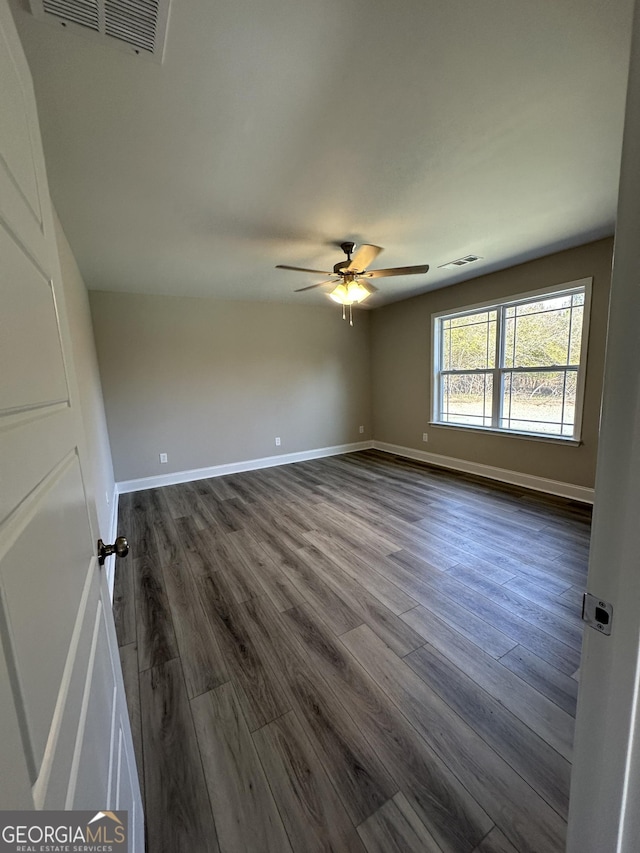 empty room featuring visible vents, dark wood-type flooring, and baseboards