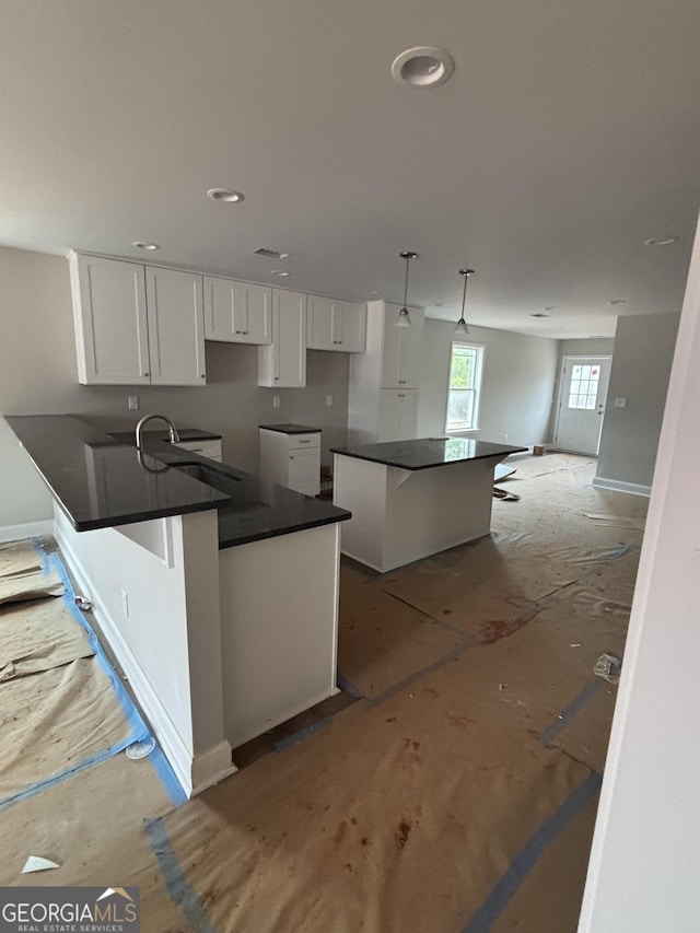 kitchen featuring a sink, dark countertops, white cabinetry, a peninsula, and baseboards