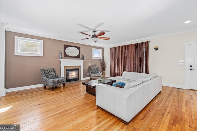 living room with light wood-style flooring, baseboards, crown molding, and a fireplace with flush hearth