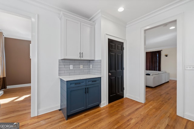 kitchen with crown molding, light wood finished floors, tasteful backsplash, light countertops, and white cabinets