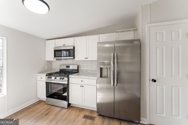 kitchen featuring white cabinetry, lofted ceiling, appliances with stainless steel finishes, and backsplash