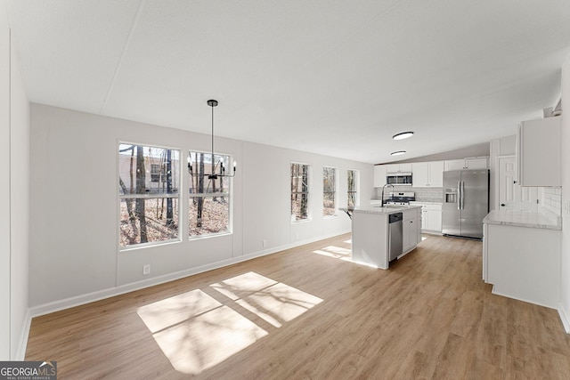 kitchen featuring appliances with stainless steel finishes, an island with sink, decorative backsplash, hanging light fixtures, and light hardwood / wood-style flooring