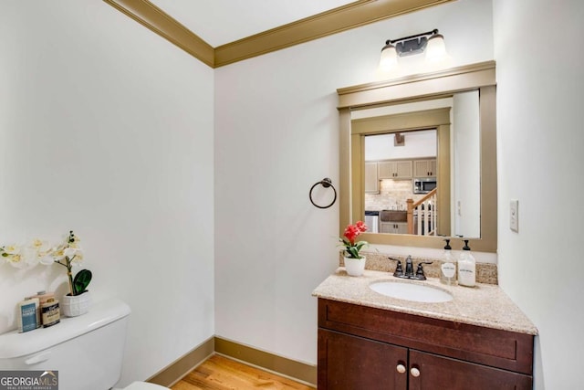 bathroom with tasteful backsplash, hardwood / wood-style flooring, vanity, ornamental molding, and toilet