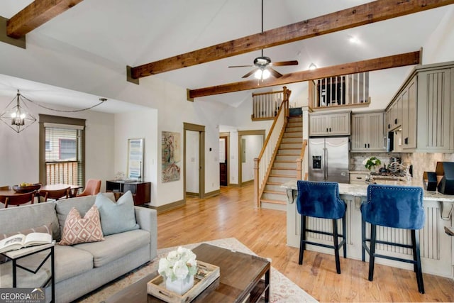 living room with ceiling fan with notable chandelier, high vaulted ceiling, beam ceiling, and light hardwood / wood-style floors