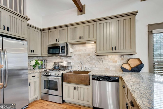 kitchen featuring tasteful backsplash, sink, light stone countertops, and appliances with stainless steel finishes