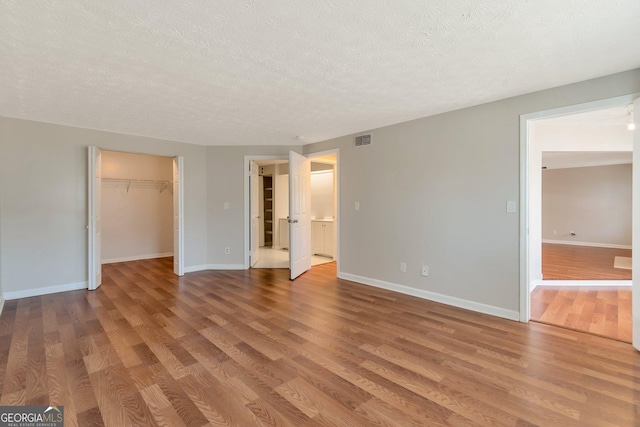 unfurnished bedroom featuring connected bathroom, hardwood / wood-style flooring, a textured ceiling, and a spacious closet