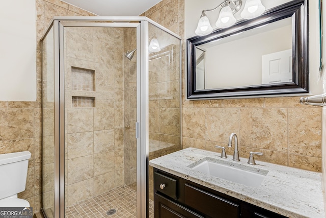 bathroom featuring vanity, a shower with shower door, tile walls, and toilet