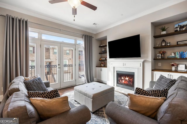 living room with french doors, a premium fireplace, ceiling fan, built in features, and crown molding