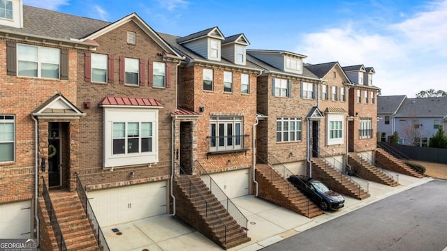 multi unit property featuring stairway, an attached garage, a residential view, concrete driveway, and brick siding