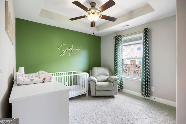 bedroom with a tray ceiling, ceiling fan, a crib, and carpet floors