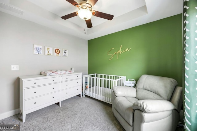 carpeted bedroom featuring a raised ceiling, ceiling fan, and a crib