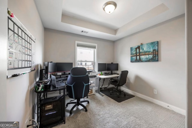 carpeted home office with a tray ceiling