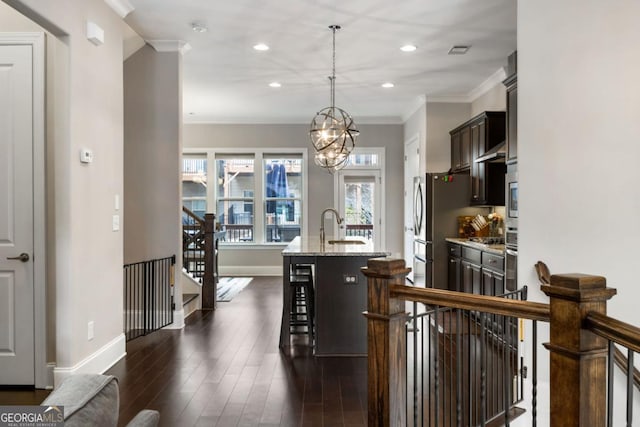 kitchen with a kitchen bar, hanging light fixtures, an island with sink, dark brown cabinets, and light stone countertops