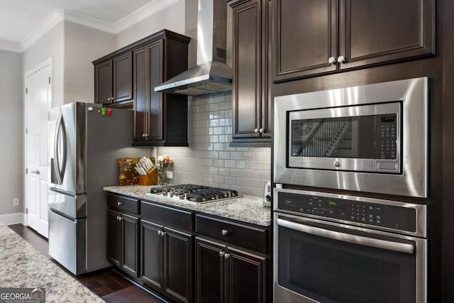 kitchen with wall chimney exhaust hood, stainless steel appliances, crown molding, and light stone countertops