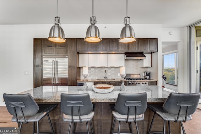 kitchen featuring dark brown cabinets, appliances with stainless steel finishes, a kitchen island, and ventilation hood