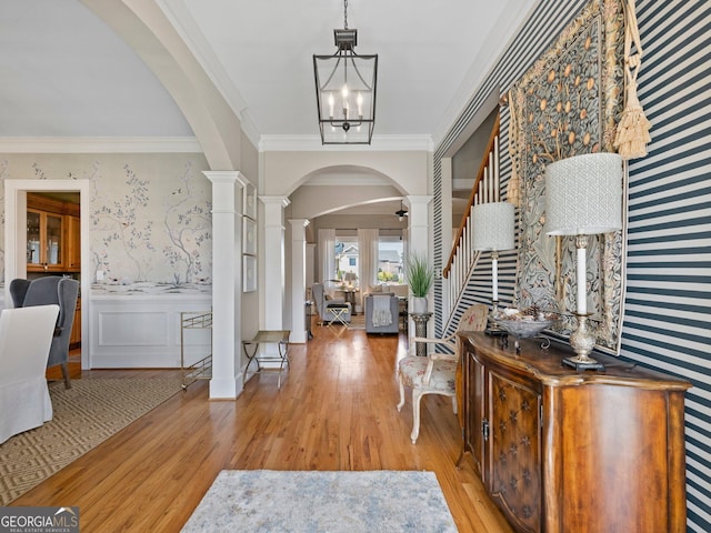 foyer entrance featuring an inviting chandelier, crown molding, light wood-type flooring, and ornate columns