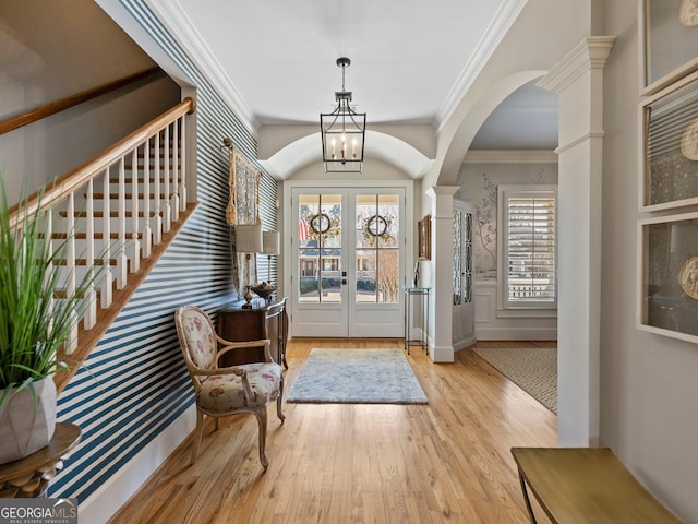 foyer entrance featuring a notable chandelier, ornamental molding, light hardwood / wood-style floors, and french doors