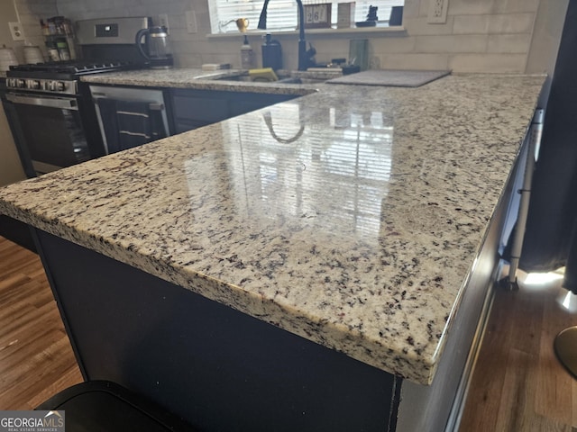 kitchen featuring dark wood-type flooring, sink, stainless steel gas range oven, light stone counters, and decorative backsplash