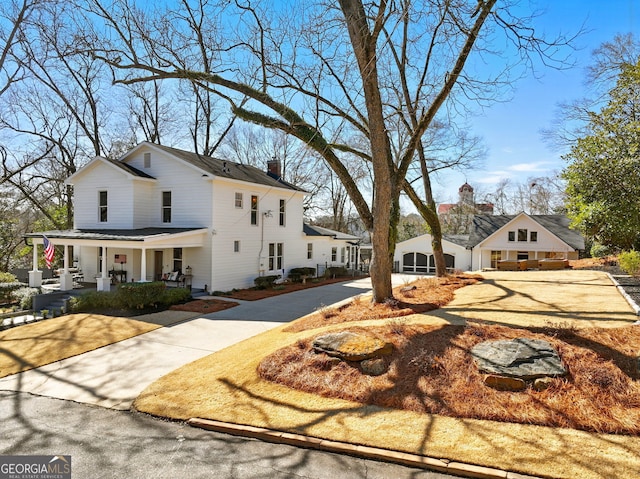 view of front of house with covered porch, a chimney, and concrete driveway