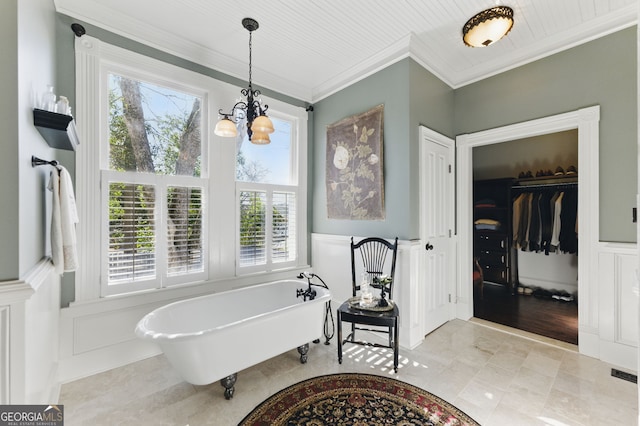 bathroom featuring wainscoting, ornamental molding, an inviting chandelier, a freestanding tub, and a decorative wall