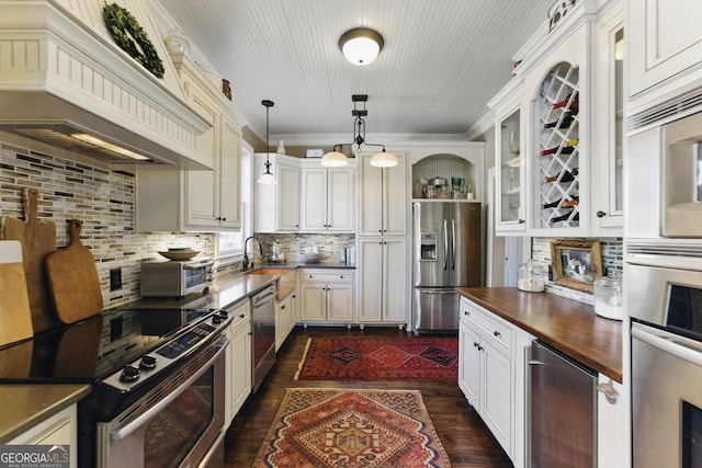 kitchen featuring custom exhaust hood, butcher block counters, appliances with stainless steel finishes, glass insert cabinets, and beverage cooler