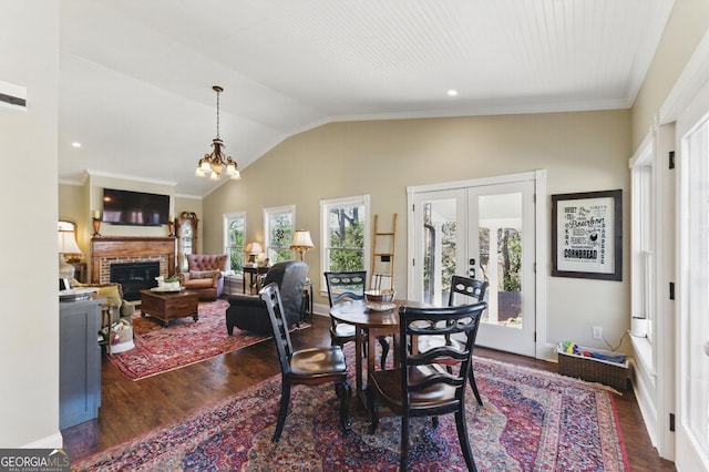 dining room with lofted ceiling, a notable chandelier, dark wood-type flooring, french doors, and a brick fireplace