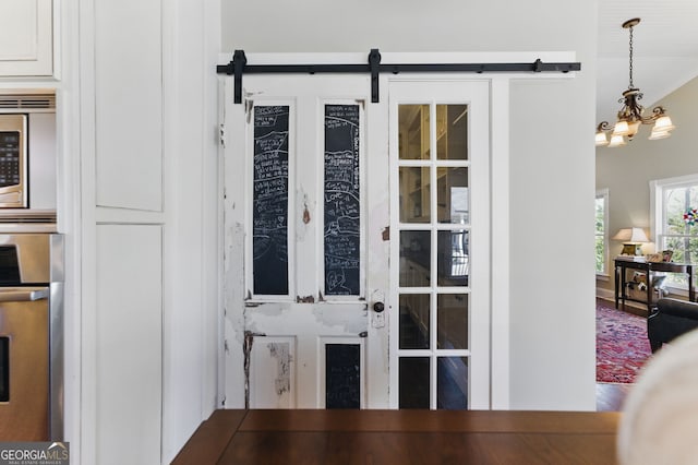 interior space featuring a notable chandelier, stainless steel appliances, wood finished floors, and a barn door