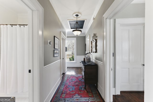 corridor featuring a wainscoted wall, visible vents, dark wood finished floors, and ornamental molding