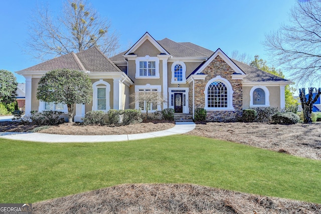 view of front of home with a shingled roof, a front yard, stone siding, and stucco siding