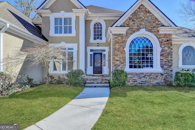 view of front of house with a front yard, stone siding, and stucco siding