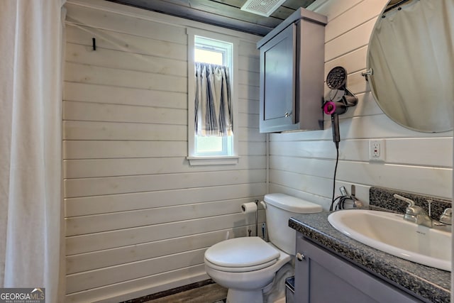 bathroom featuring vanity, plenty of natural light, toilet, and wood walls