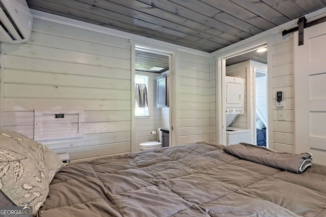 bedroom featuring stacked washer / drying machine, ensuite bathroom, wood ceiling, a wall mounted air conditioner, and a barn door