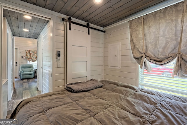 bedroom featuring wood ceiling, a barn door, hardwood / wood-style floors, and wood walls