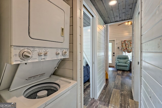 clothes washing area with dark wood-type flooring, wood ceiling, stacked washer / dryer, and wooden walls