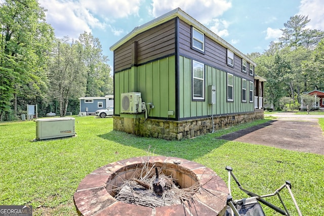 view of side of property with a fire pit, a lawn, and ac unit