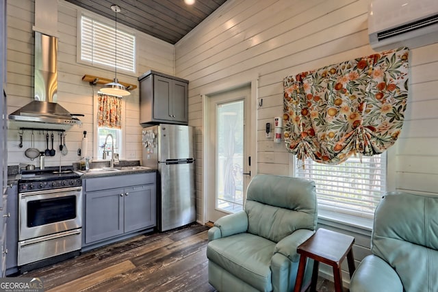 kitchen featuring pendant lighting, wall chimney range hood, stainless steel appliances, a wall mounted AC, and wood walls