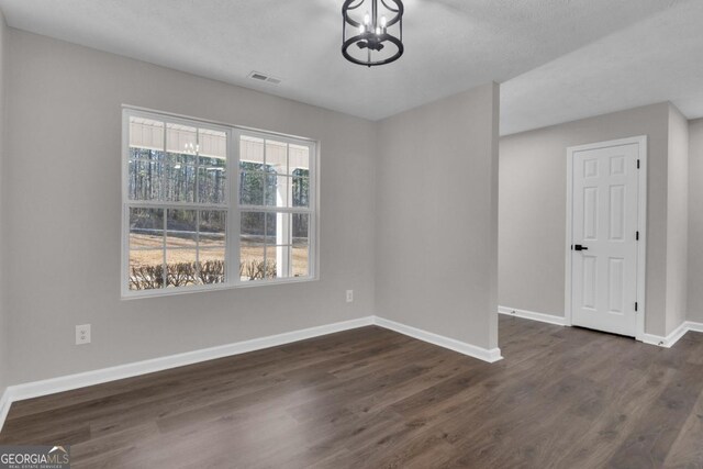 unfurnished room with an inviting chandelier, dark wood-type flooring, and a textured ceiling