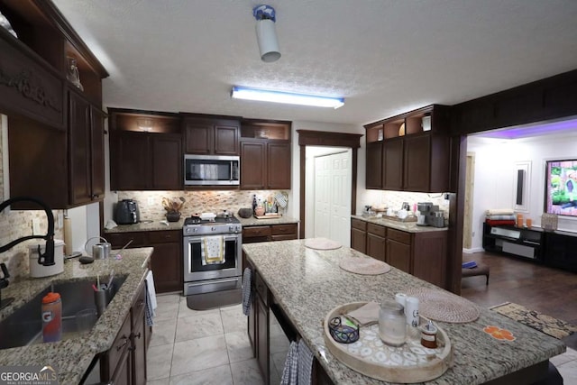 kitchen with sink, appliances with stainless steel finishes, backsplash, dark brown cabinets, and light stone counters